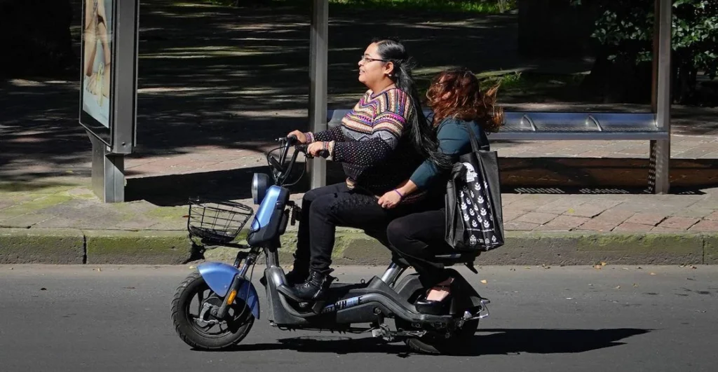 Dos personas circulando en una bicimoto eléctrica azul en la Ciudad de México, ejemplo de vehículo que requiere placas y licencia.