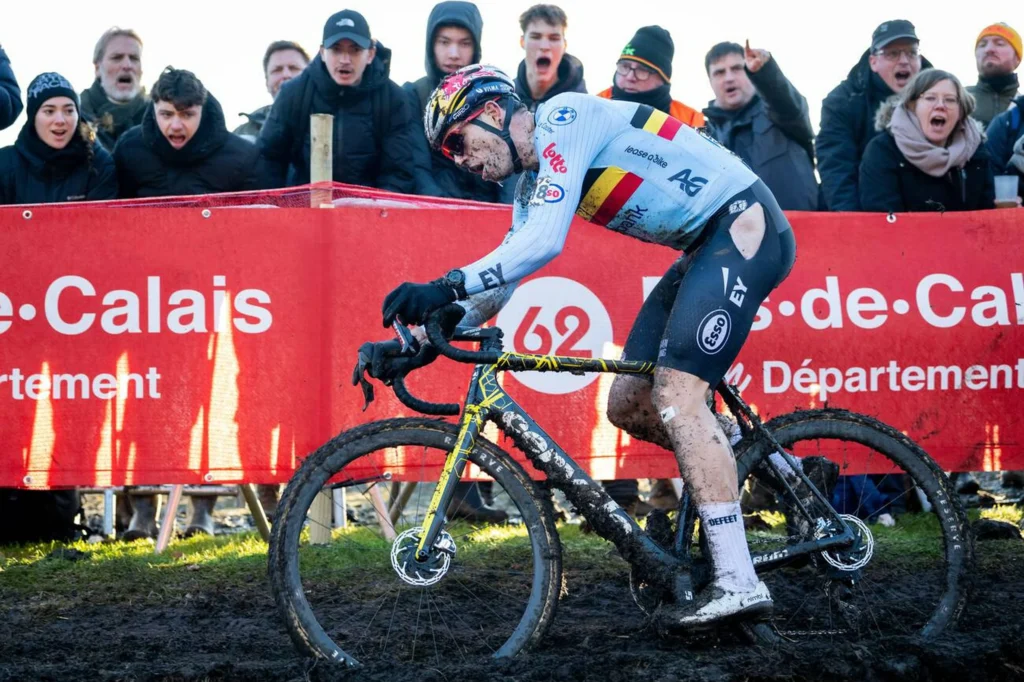 Competencia de ciclocross con ciclista profesional belga enfrentando un tramo de barro frente al público