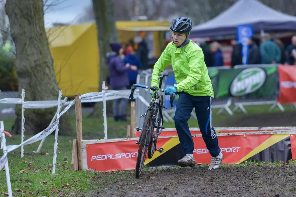 Competidor aficionado de ciclismo en barro superando obstáculos con su bicicleta en mano