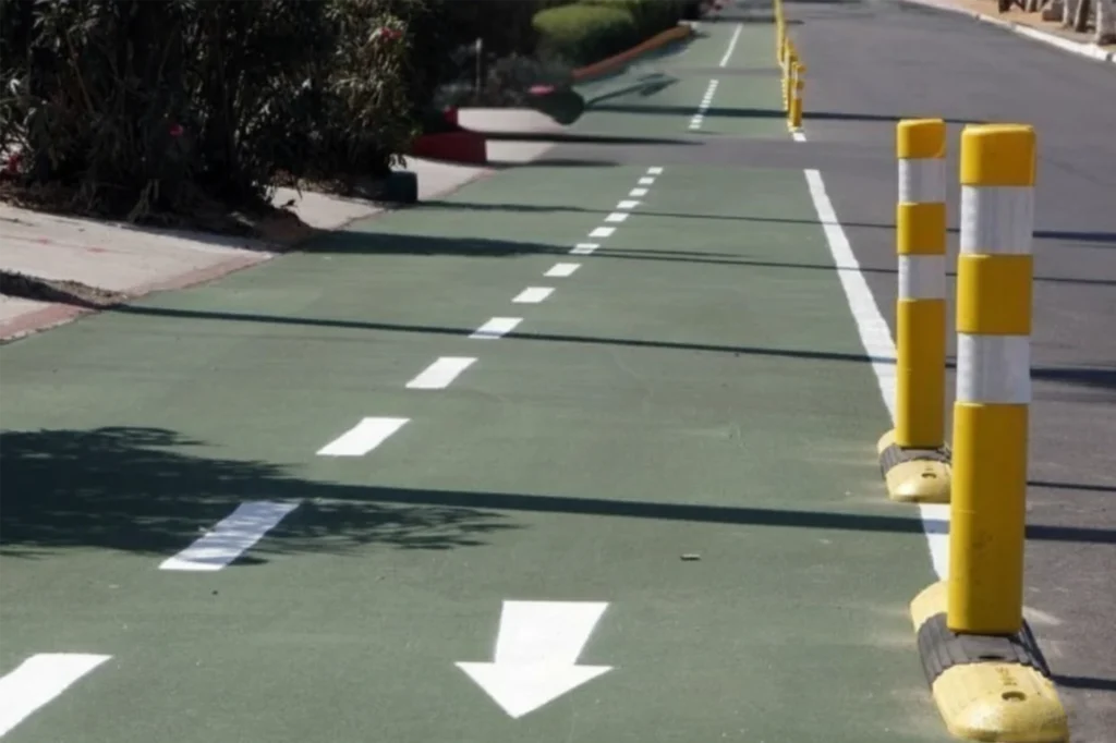 Carril bici en Baja California Sur con delimitadores amarillos y señalización horizontal blanca sobre pavimento verde, diseñado para uso seguro de ciclistas urbanos.